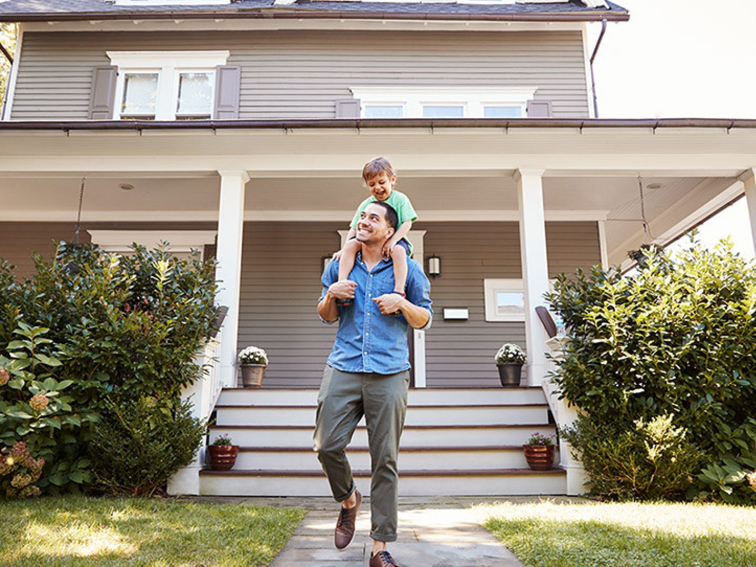 Father with his child on his shoulders outside their new home.