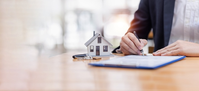 Man signs paper document next to model of a house.